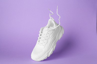 Photo of Stylish white sneaker in air against violet background