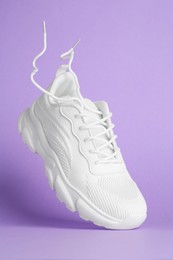 Photo of Stylish white sneaker in air against violet background