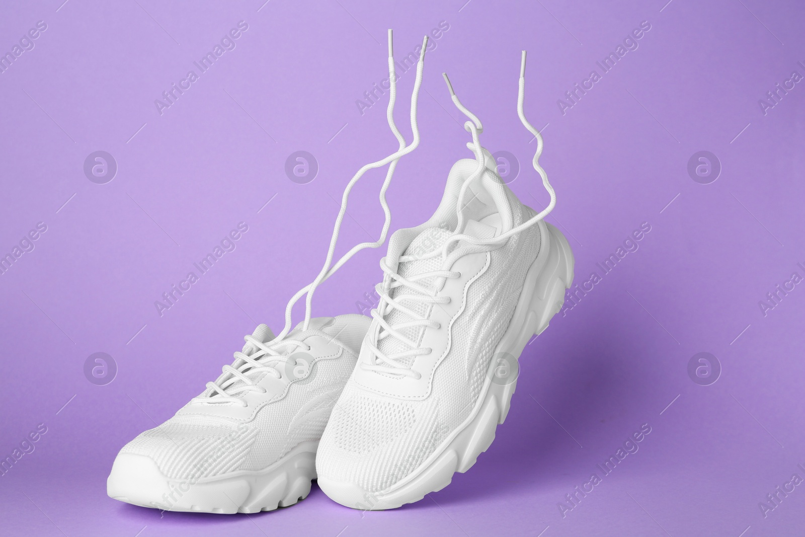 Photo of Pair of stylish white sneakers in air against violet background