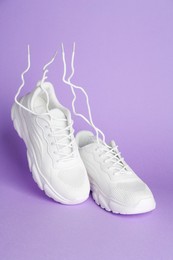 Photo of Pair of stylish white sneakers in air against violet background