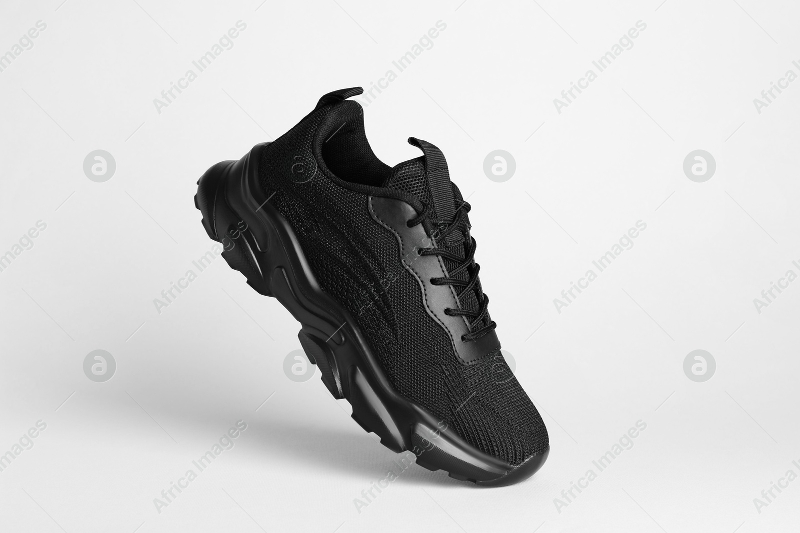 Photo of Stylish black sneaker in air against white background