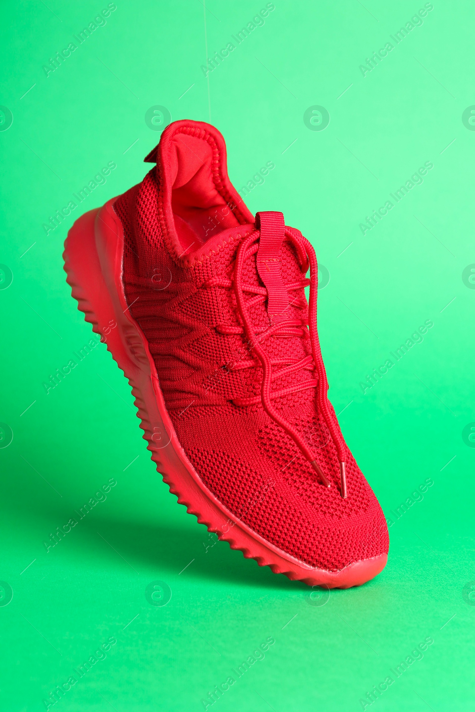 Photo of Stylish red sneaker in air against green background