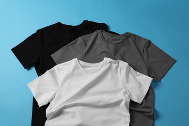 Photo of Blank t-shirts on light blue background, flat lay. Mockup for design