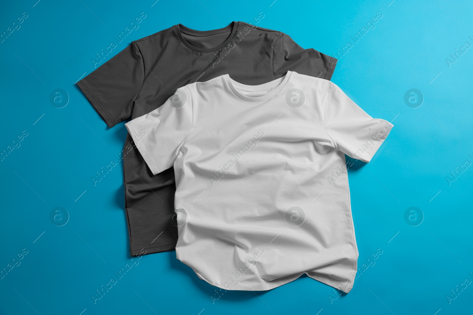 Photo of Blank t-shirts on light blue background, flat lay. Mockup for design