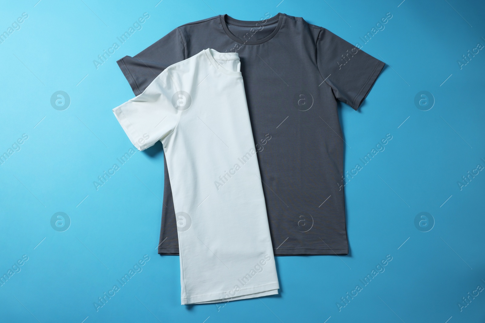 Photo of Blank t-shirts on light blue background, flat lay. Mockup for design