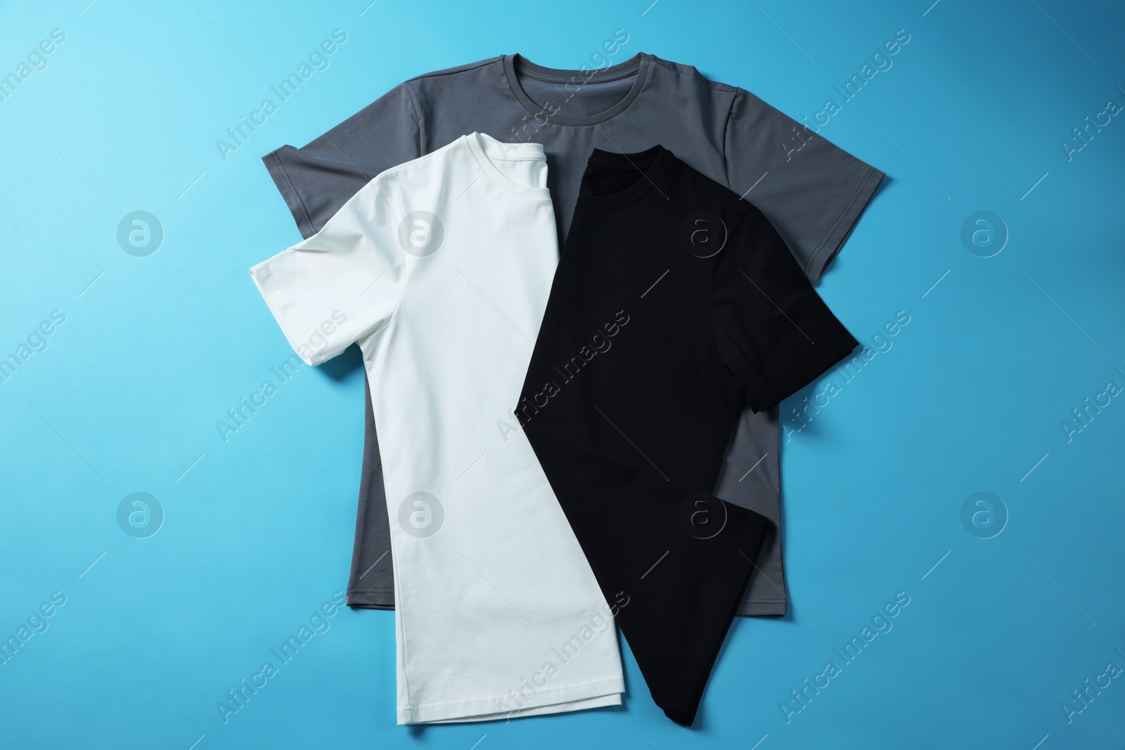 Photo of Blank t-shirts on light blue background, flat lay. Mockup for design