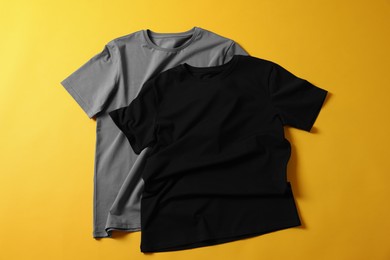 Photo of Blank t-shirts on yellow background, flat lay. Mockup for design