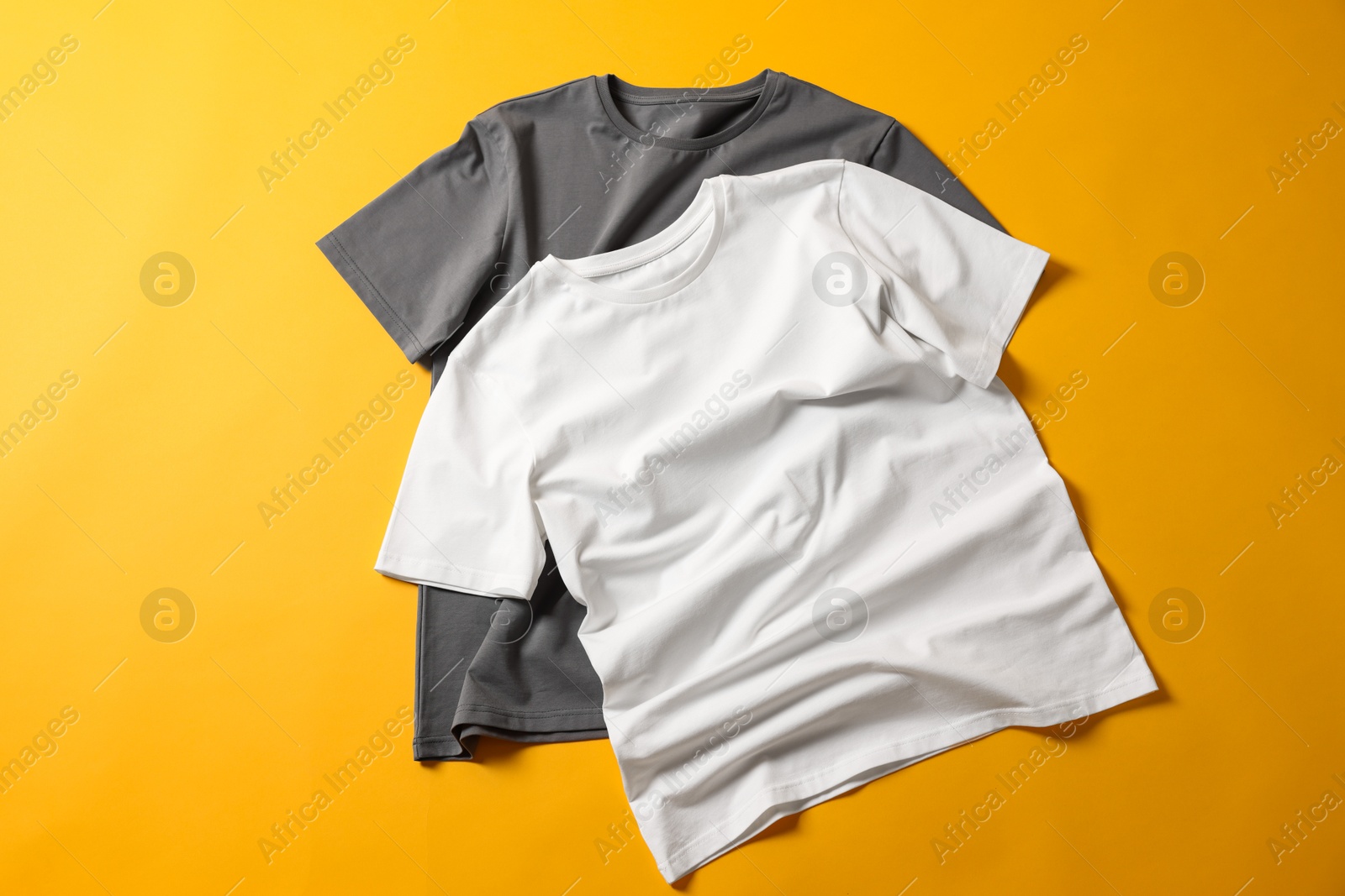 Photo of Blank t-shirts on yellow background, flat lay. Mockup for design