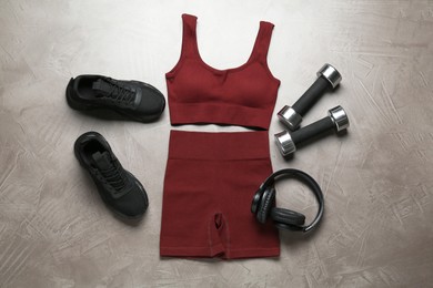 Photo of Brown sportswear, black sneakers, dumbbells and headphones on gray textured background, flat lay