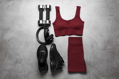 Photo of Brown sportswear, black sneakers, dumbbells and headphones on gray textured background, flat lay