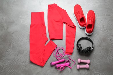 Photo of Red sportswear, sneakers, dumbbells and skipping rope on gray textured background, flat lay