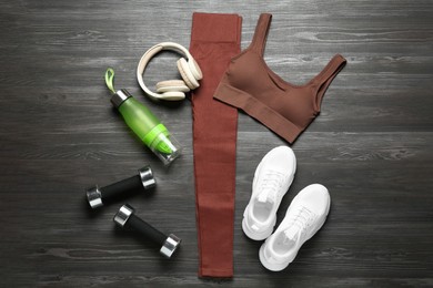 Photo of Brown sportswear, white sneakers, juicer bottle, dumbbells and headphones on wooden background, flat lay