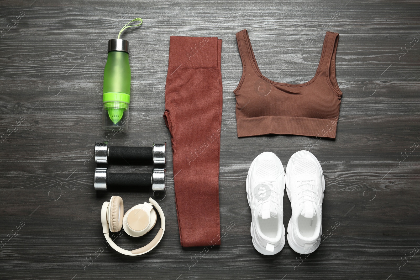 Photo of Brown sportswear, white sneakers, juicer bottle, dumbbells and headphones on wooden background, flat lay