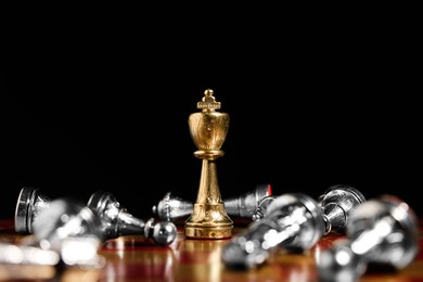 Photo of Golden chess king among fallen silver pieces on chessboard against black background, closeup. Competition concept