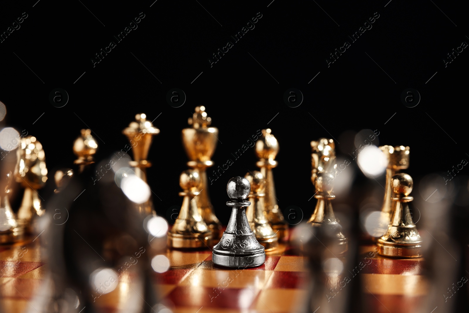 Photo of Silver pawn in front of golden chess pieces on chessboard against black background, closeup. Competition concept