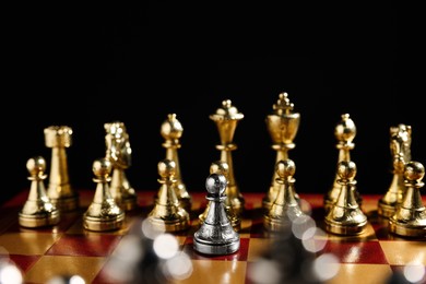 Photo of Silver pawn in front of golden chess pieces on chessboard against black background, closeup. Competition concept