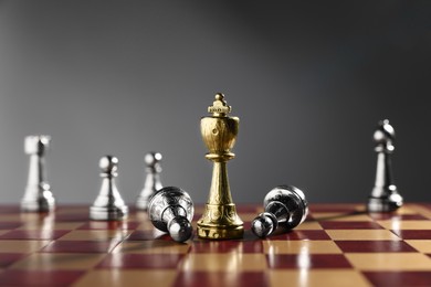 Photo of Golden chess king among fallen silver pieces on chessboard against grey background, closeup. Competition concept