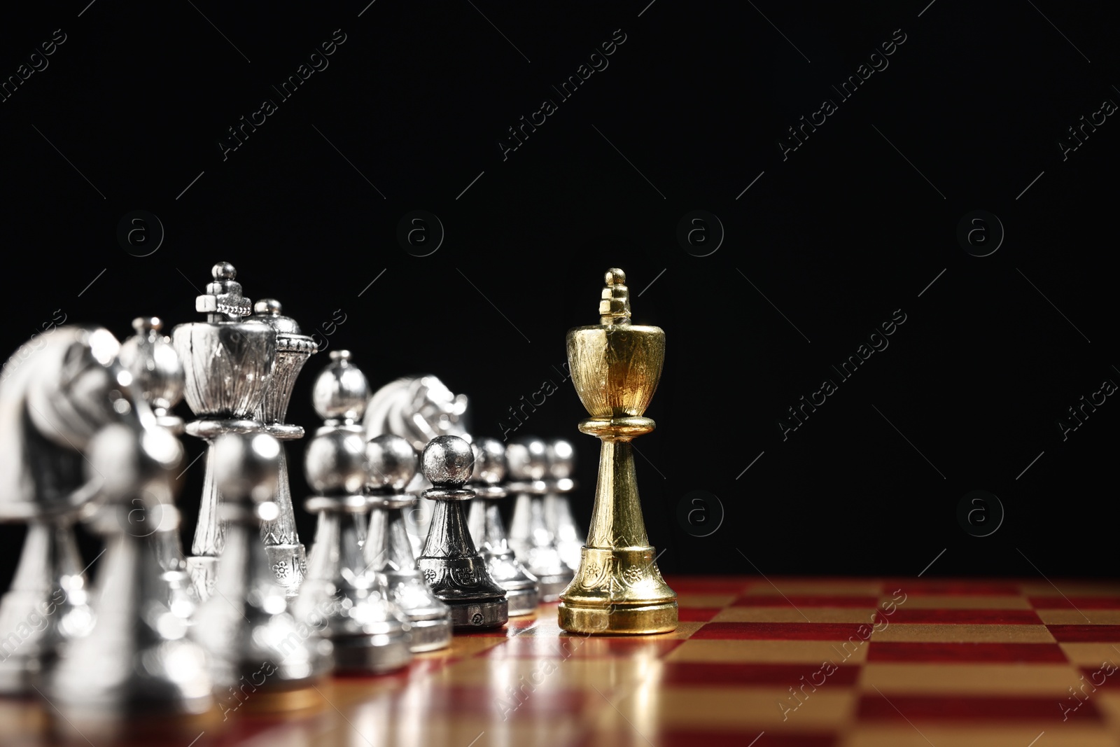 Photo of Golden king in front of silver chess pieces on chessboard against black background, closeup and space for text. Competition concept