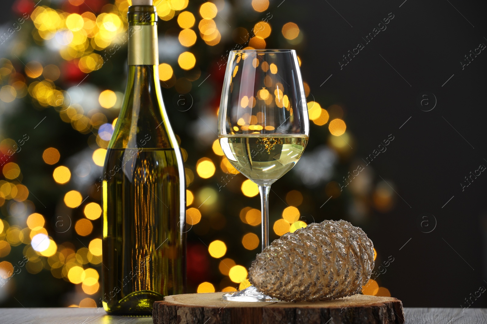 Photo of Wine in glass, bottle and Christmas decor on wooden table against blurred lights, closeup