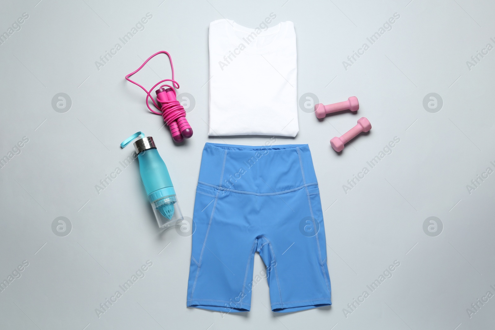 Photo of Stylish sportswear, juicer bottle, dumbbells and skipping rope on light background, flat lay