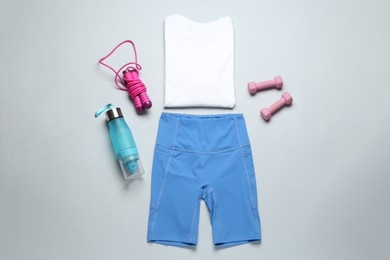 Photo of Stylish sportswear, juicer bottle, dumbbells and skipping rope on light background, flat lay