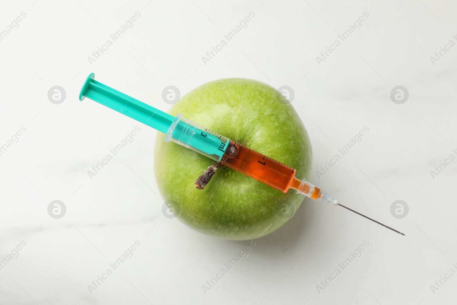 Photo of GMO concept. Green apple and syringe on white marble table, top view