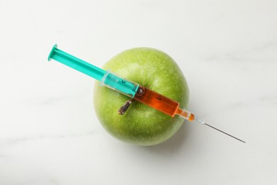 Photo of GMO concept. Green apple and syringe on white marble table, top view