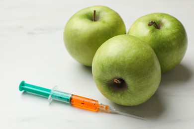 Photo of GMO concept. Green apples and syringe on white marble table, closeup