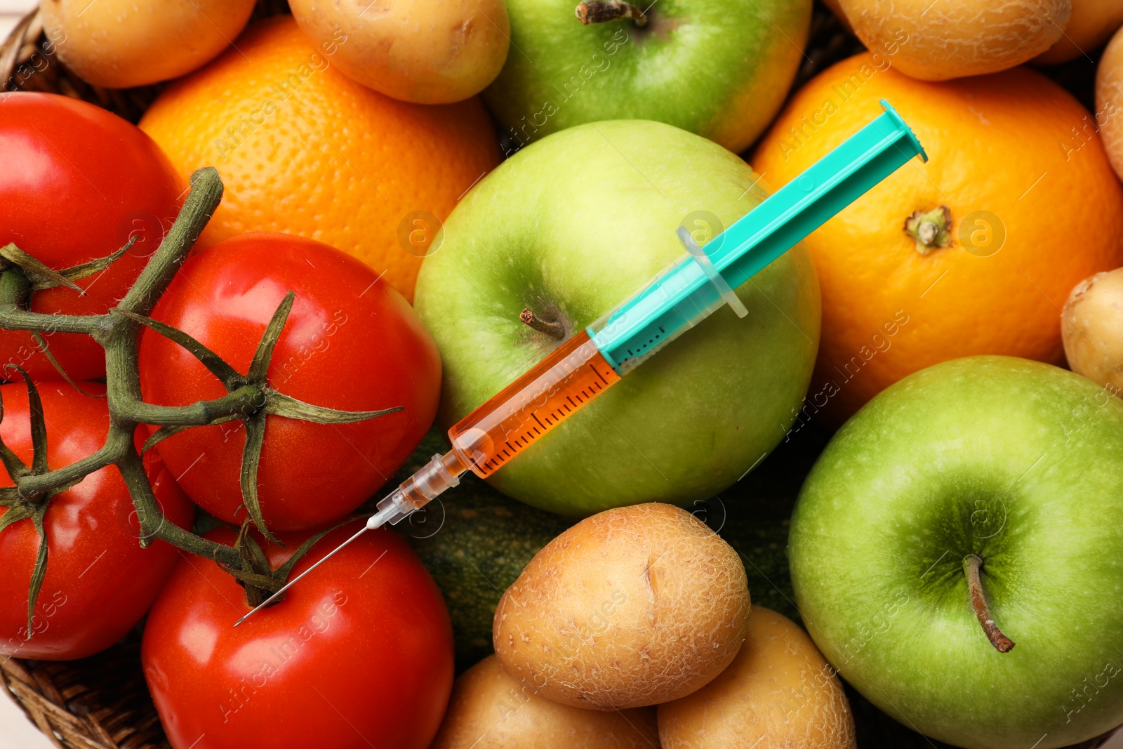 Photo of GMO concept. Different vegetables, fruits and syringe in basket, top view