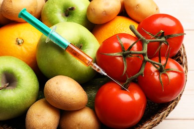 Photo of GMO concept. Different vegetables, fruits and syringe in basket on table, closeup