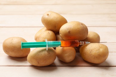 Photo of GMO concept. Potatoes and syringe on wooden table, closeup