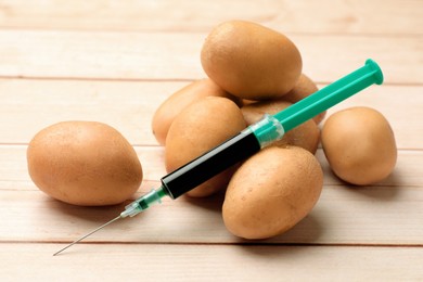 Photo of GMO concept. Potatoes and syringe on wooden table, closeup