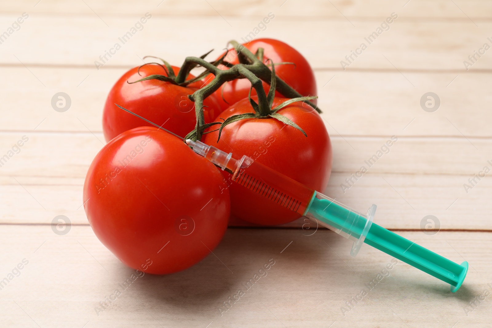 Photo of GMO concept. Fresh tomatoes and syringe on wooden table, closeup