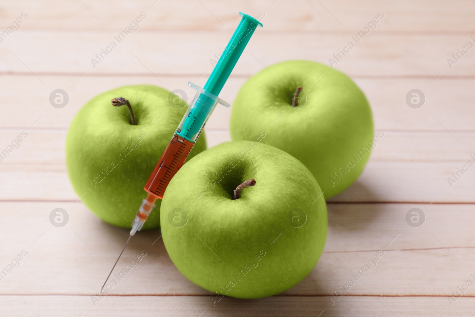 Photo of GMO concept. Fresh apples and syringe on wooden table, closeup