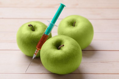 Photo of GMO concept. Fresh apples and syringe on wooden table, closeup