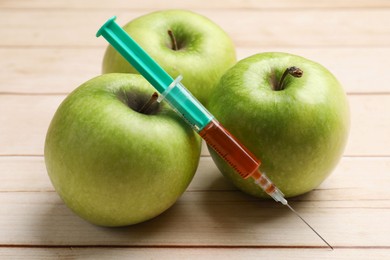 Photo of GMO concept. Fresh apples and syringe on wooden table, closeup