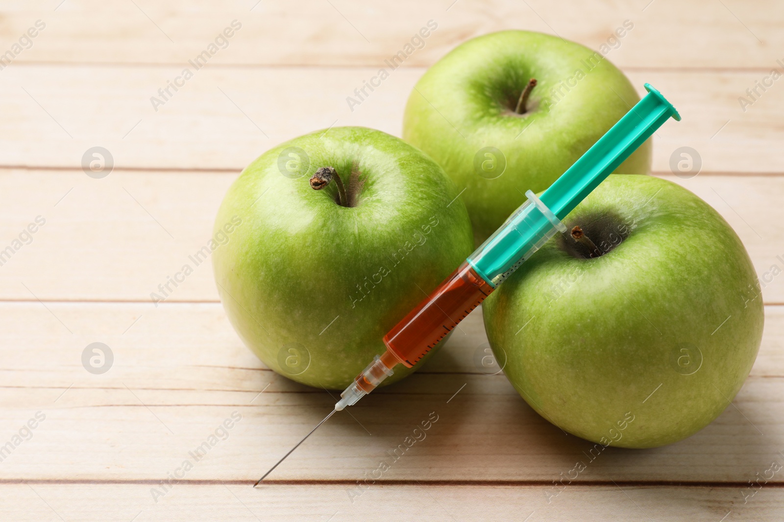 Photo of GMO concept. Fresh apples and syringe on wooden table, closeup. Space for text