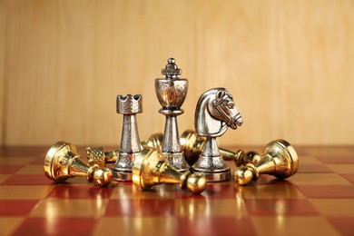 Photo of Silver chess pieces among fallen golden ones on chessboard. Competition concept