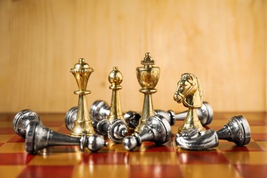 Photo of Golden chess pieces among fallen silver ones on chessboard. Competition concept