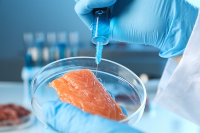 Photo of GMO concept. Scientist injecting something into piece of salmon in laboratory, closeup