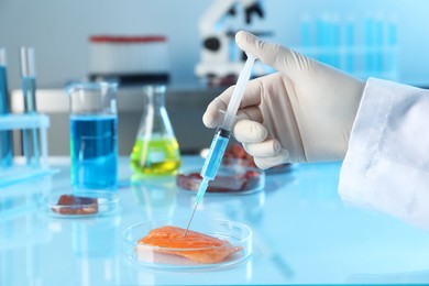 Photo of GMO concept. Scientist injecting something into piece of salmon at table in laboratory, closeup