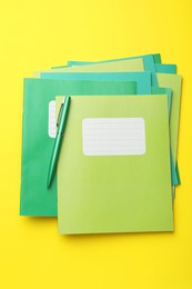 Photo of Stack of copybooks and pen on yellow background, top view