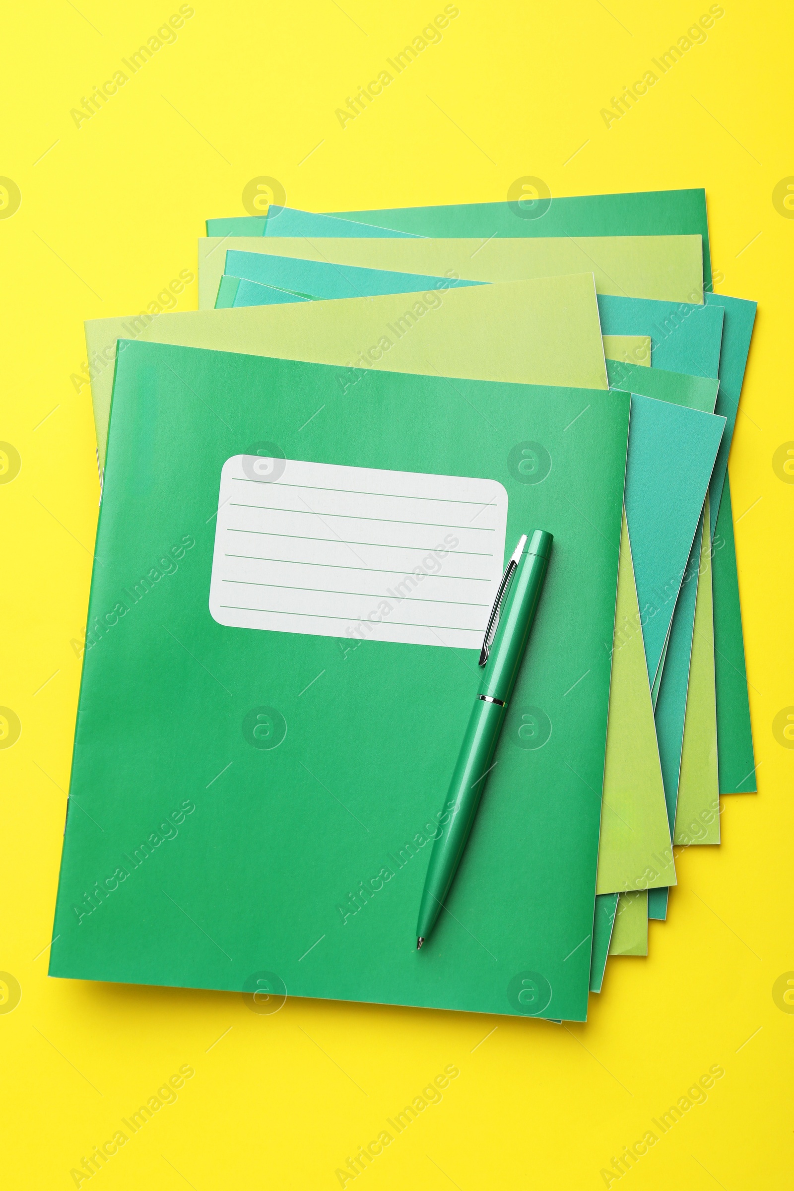 Photo of Stack of copybooks and pen on yellow background, top view