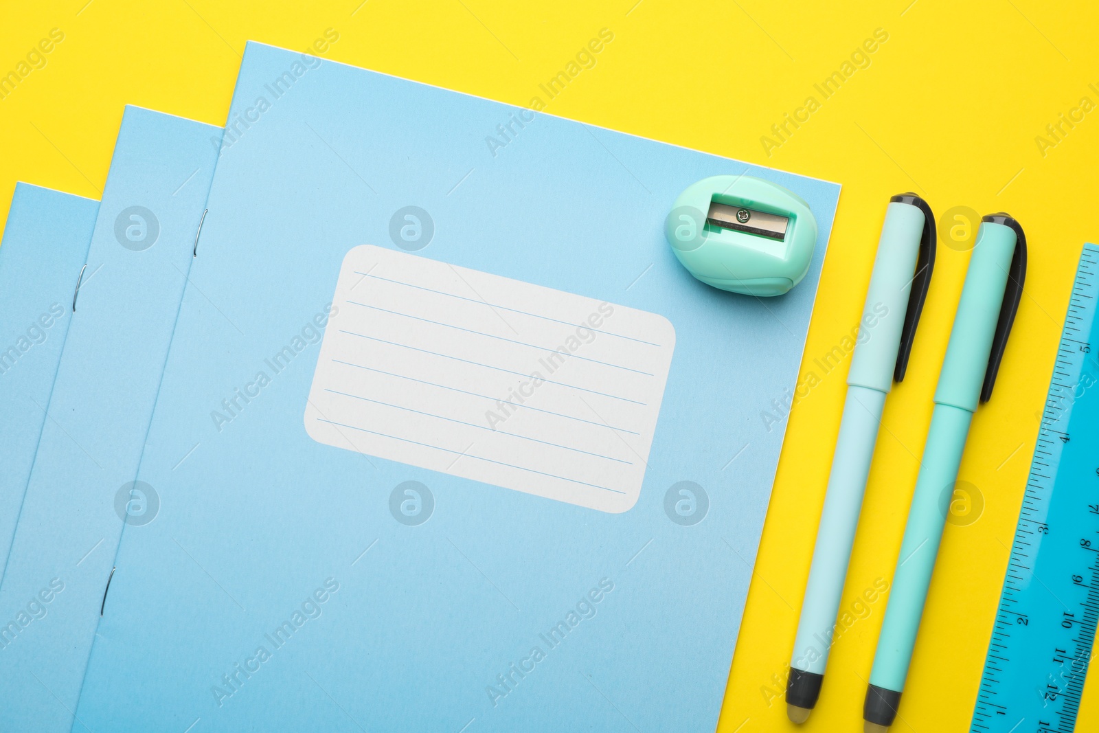 Photo of Stack of copybooks, pens, ruler and sharpener on yellow background, flat lay