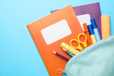 Photo of Colorful copybooks and pencil case with school stationery on light blue background, flat lay