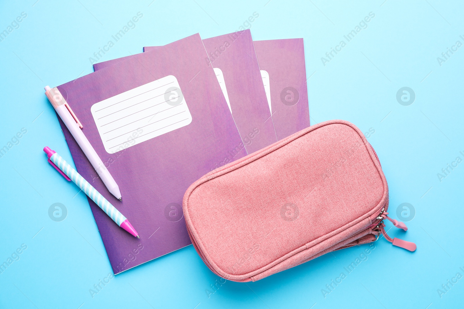 Photo of Copybooks, pens and pencil case on light blue background, flat lay