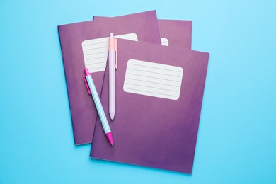 Photo of Copybooks and pens on light blue background, top view