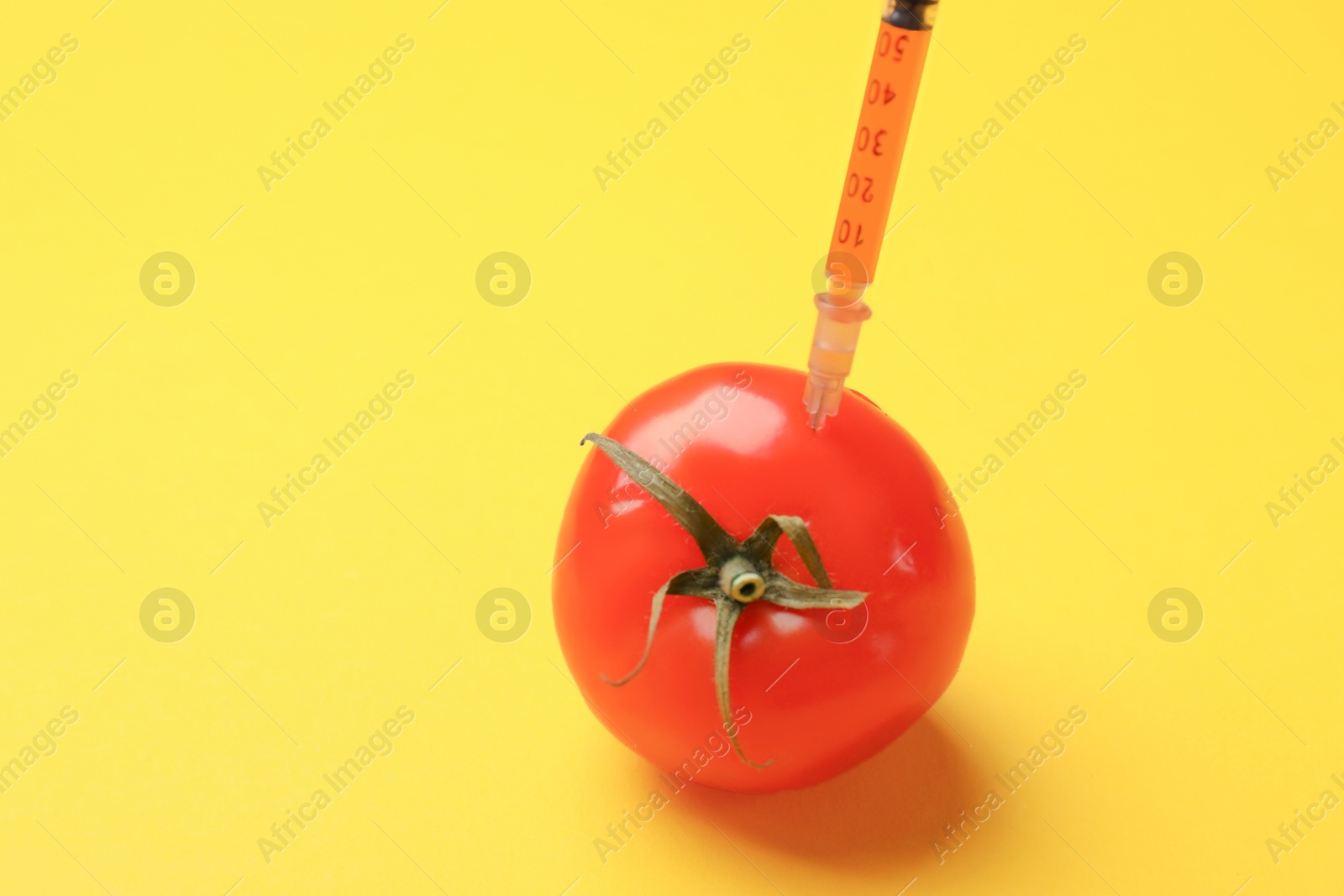 Photo of GMO concept. Tomato with syringe on yellow background, closeup. Space for text