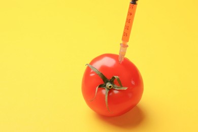 Photo of GMO concept. Tomato with syringe on yellow background, closeup. Space for text