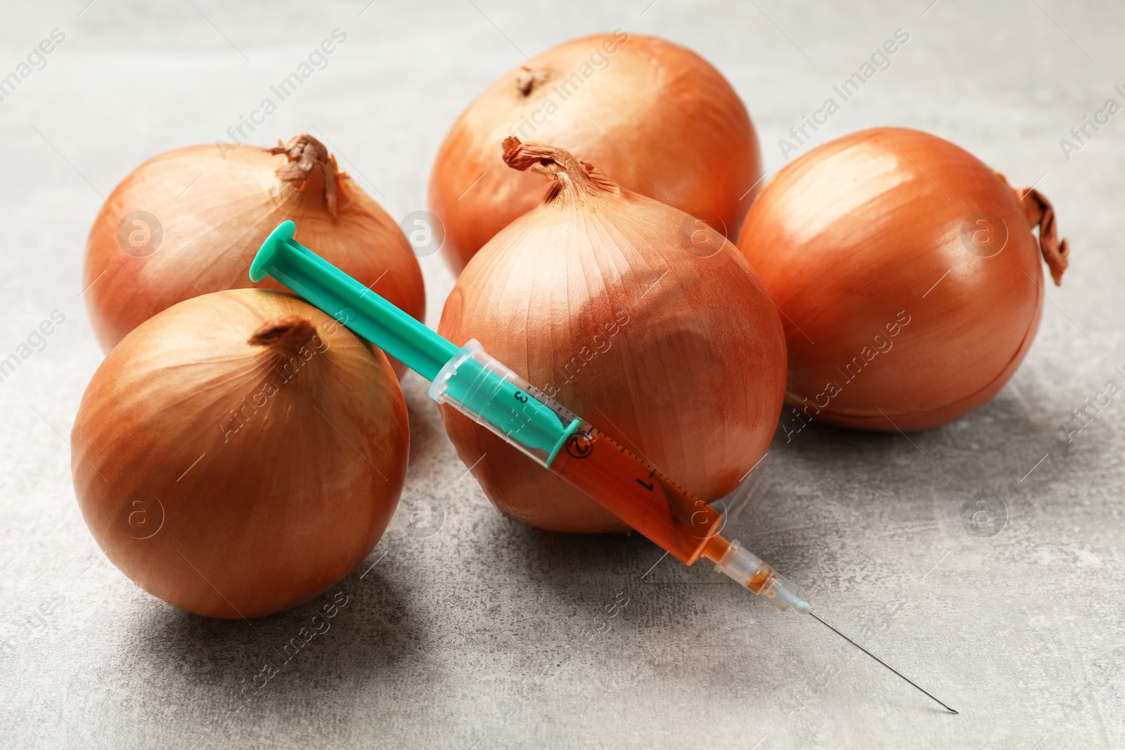 Photo of GMO concept. Onion bulbs and syringe with liquid on grey textured table, closeup